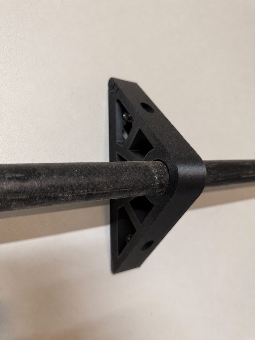 PipeHold bracket mounted on a wall, gripping a 3/4-inch black steel pipe